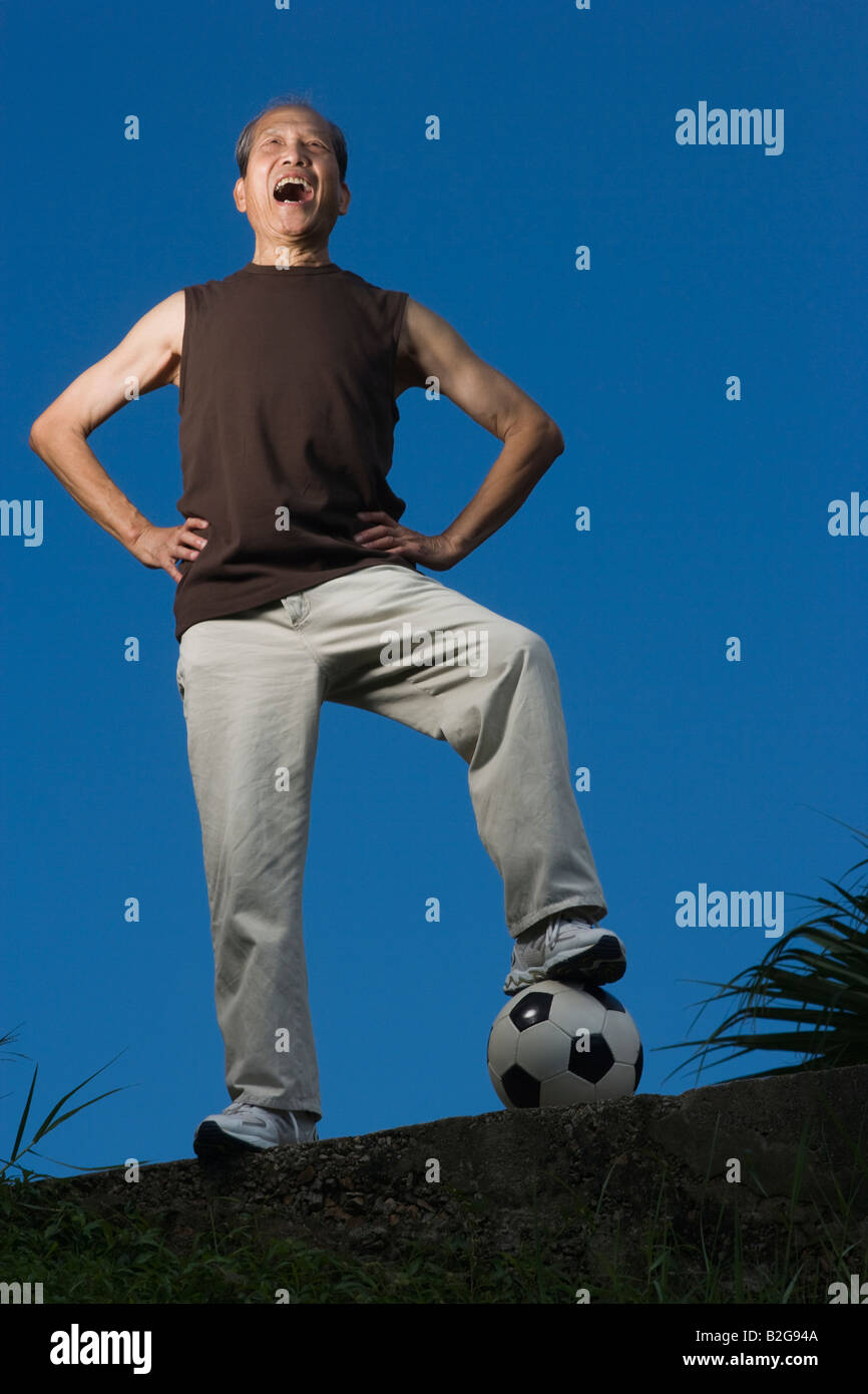 Low angle view of a senior man standing avec sa jambe sur un ballon de soccer et de crier Banque D'Images