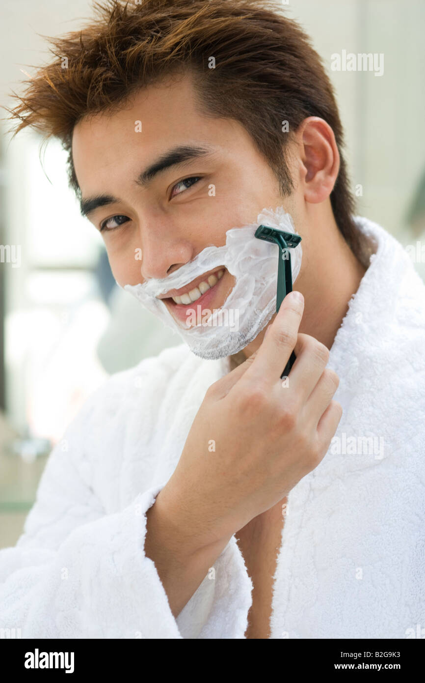 Portrait d'un jeune homme le rasage avec un rasoir et souriant Banque D'Images