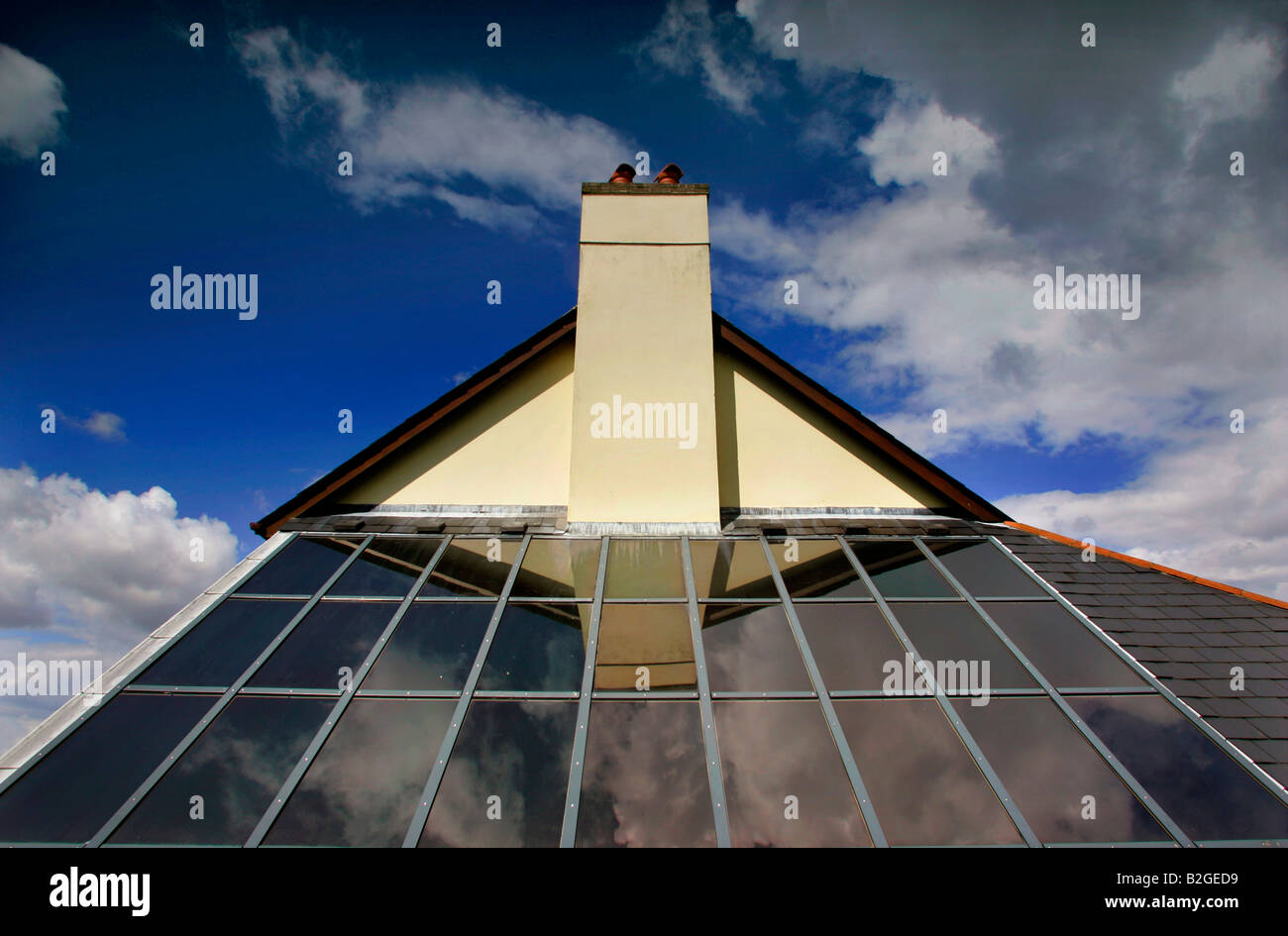 Des panneaux solaires sur un toit dans le Devon UK reflétant une toiture inclinée et la cheminée contre un ciel bleu avec des nuages. Banque D'Images