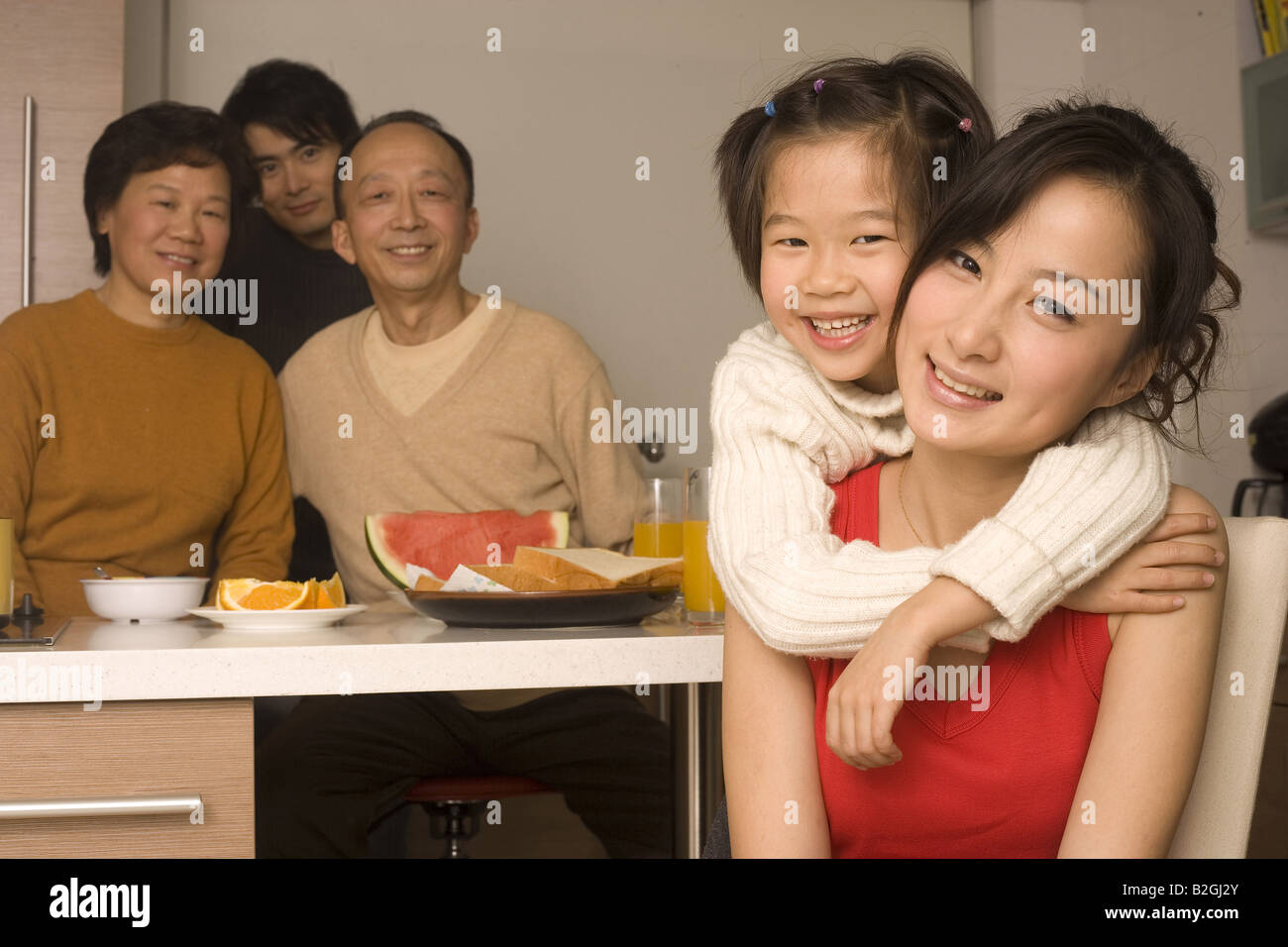 Portrait of a Girl hugging sa mère par derrière avec les membres de sa famille à la table du petit déjeuner Banque D'Images