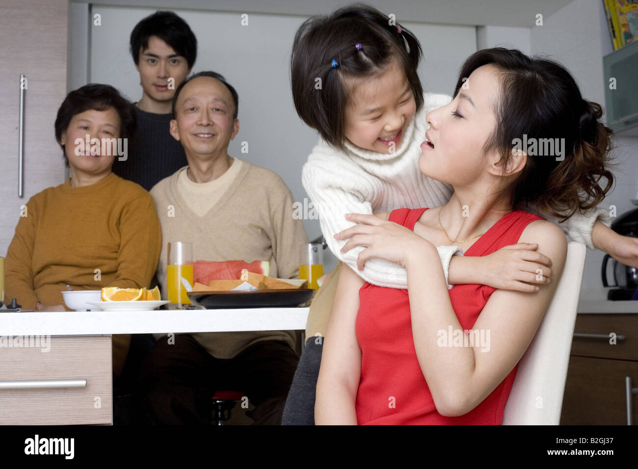 Close-up of a Girl hugging sa mère par derrière avec les membres de sa famille à la table du petit déjeuner Banque D'Images