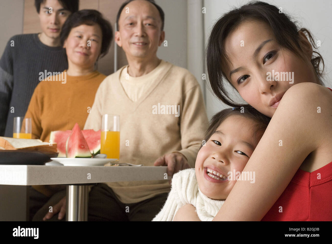 Portrait of a young woman hugging her daughter avec les membres de sa famille à la table du petit déjeuner Banque D'Images
