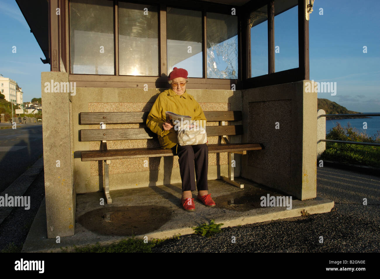 Senior woman sitting on bench in sunshine, Falmouth, Cornwall, England, UK Banque D'Images