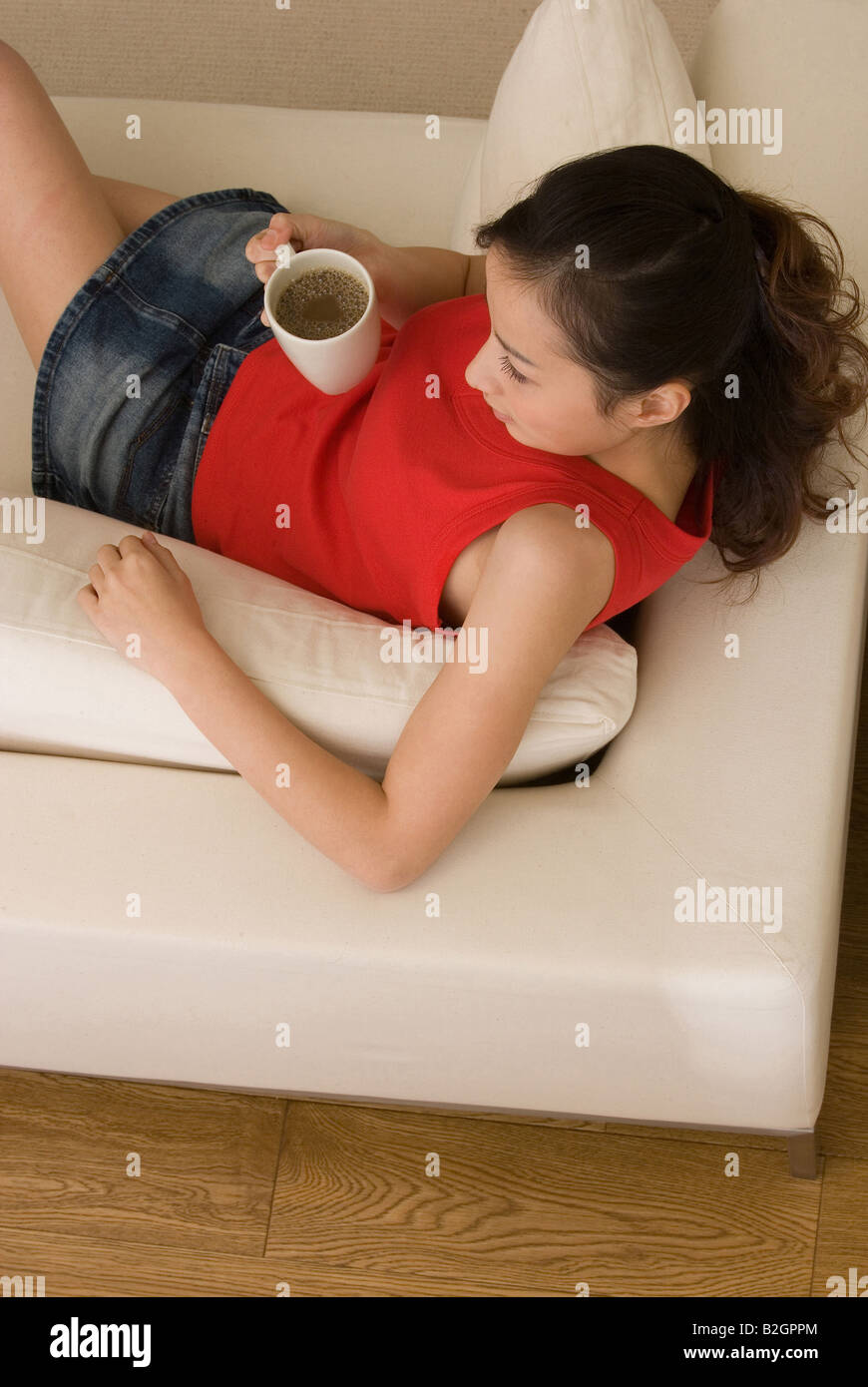 Portrait d'une jeune femme tenant une tasse de café sur un canapé Banque D'Images