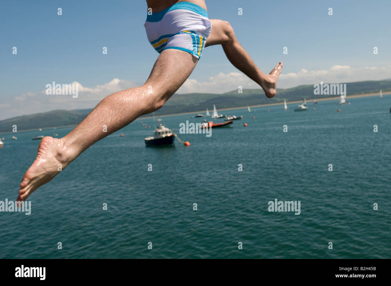 Close up des jambes d'un homme sautant au large de la jetée ou pier dans dans l'Aberdyfi Estuaire de la rivière Dyfi après-midi d'été au Pays de Galles UK Banque D'Images