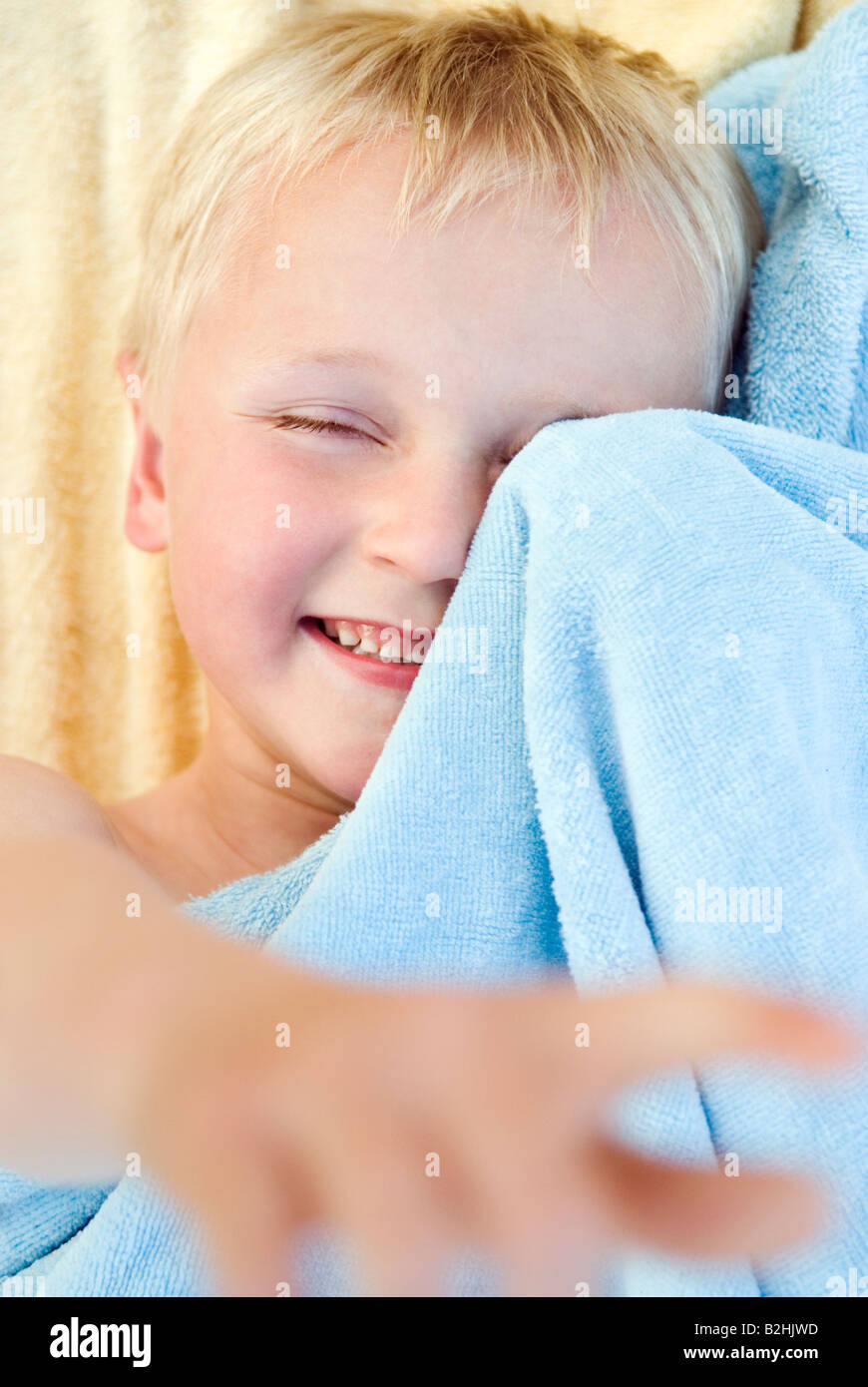 Un beau et mignon petit garçon de 6 ans s'amuse enveloppé dans sa serviette. Banque D'Images