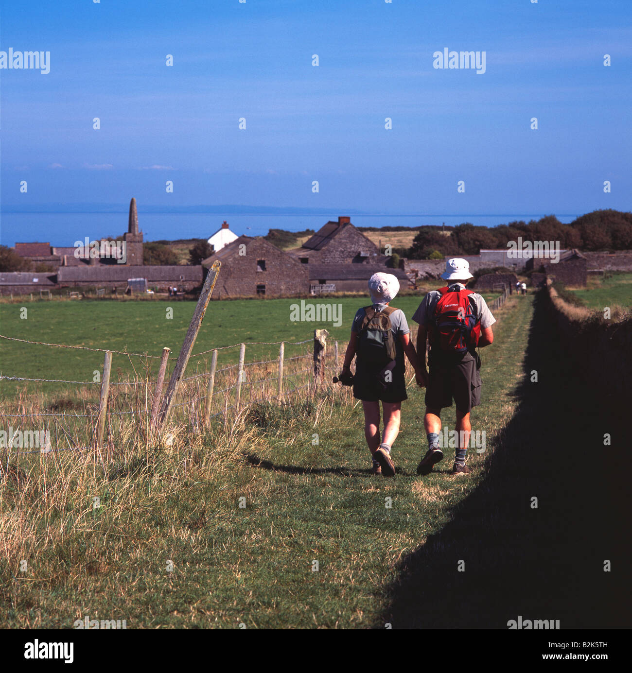 Deux personnes à marcher en direction de village sur l'île de Caldey, Pembrokeshire, avec vue sur la mer en arrière-plan Banque D'Images