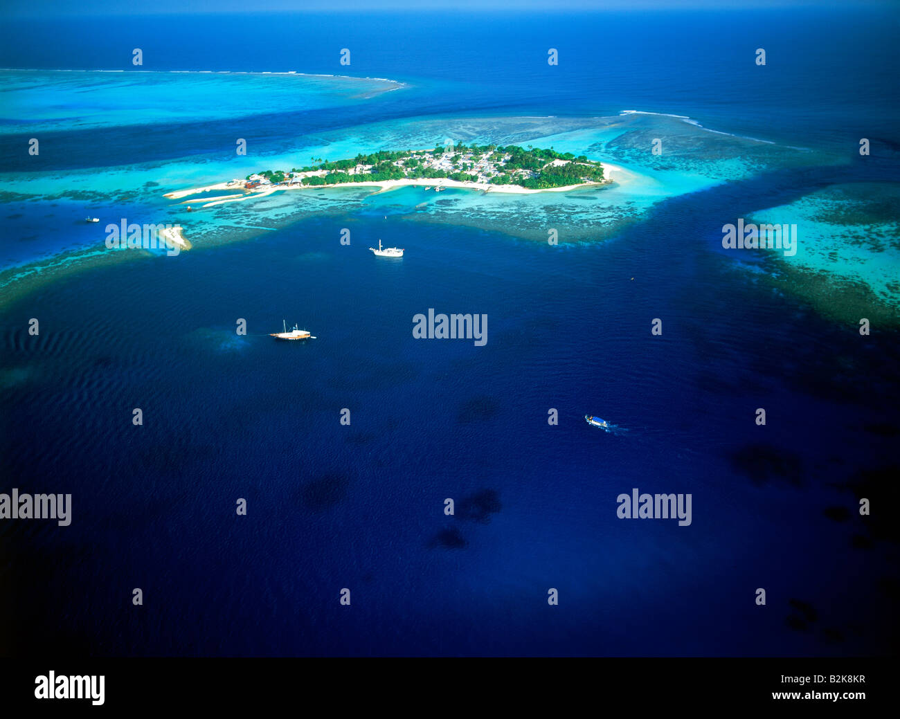 Île tropicale, encerclant des voiliers et des récifs coralliens dans les eaux bleu représentant l'île de villégiature et de vacances Banque D'Images