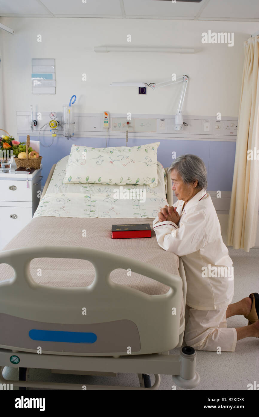 Portrait d'une femme priant à côté d'un lit à l'hôpital Banque D'Images