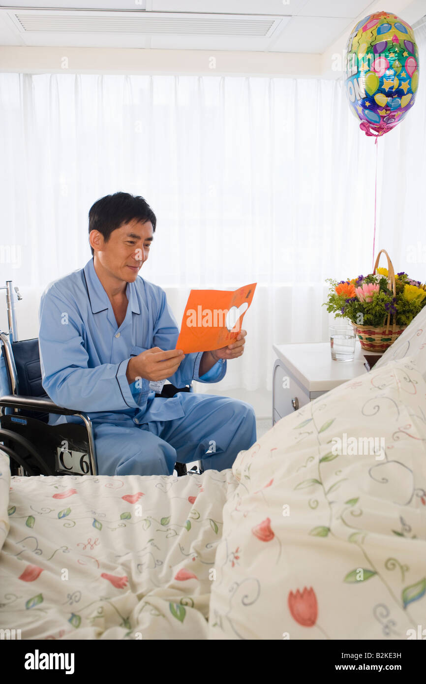 Male patient assis dans un fauteuil roulant et la lecture d'une carte de prompt rétablissement Banque D'Images