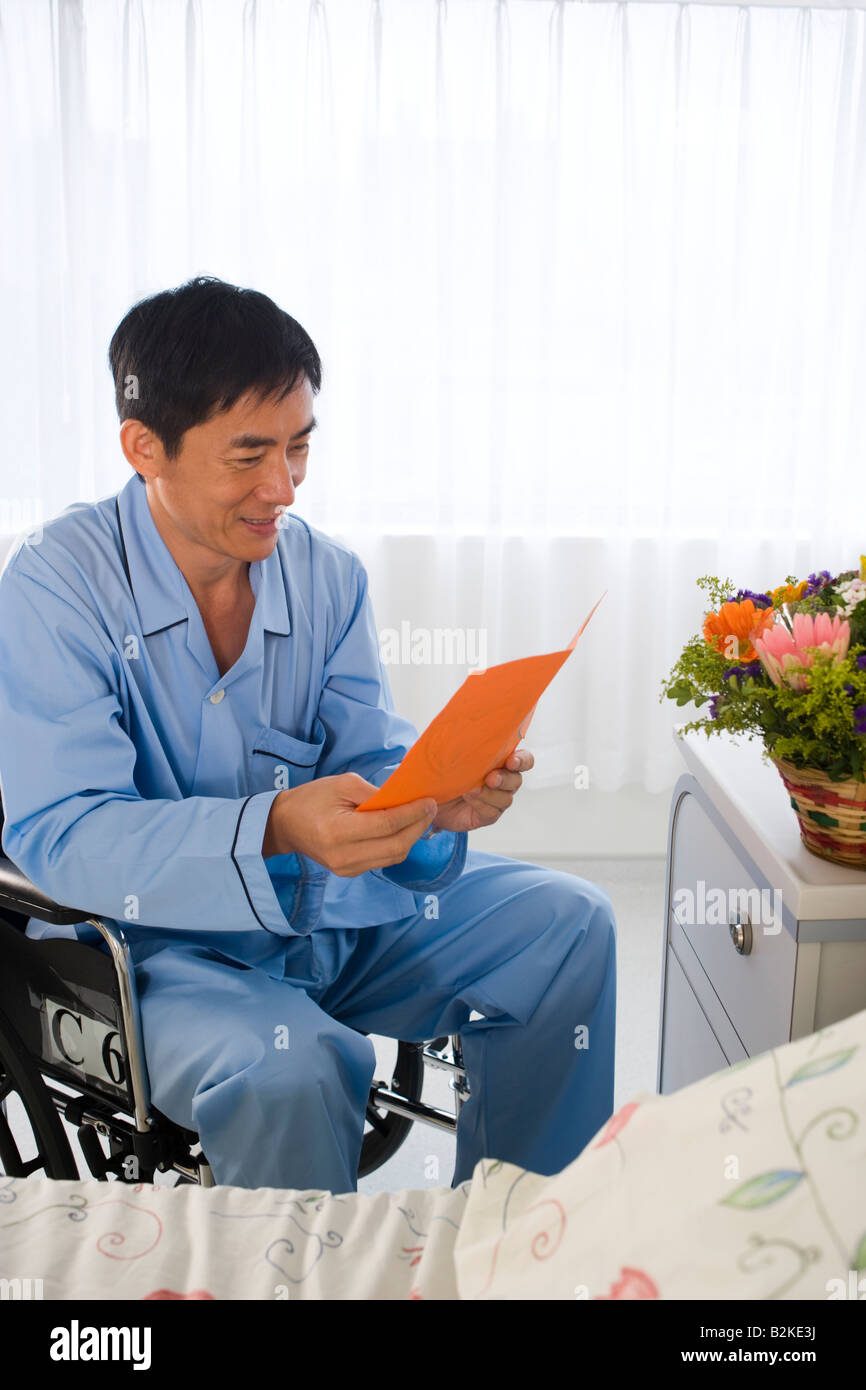 Mid adult man dans un fauteuil roulant et la lecture d'une carte de prompt rétablissement Banque D'Images