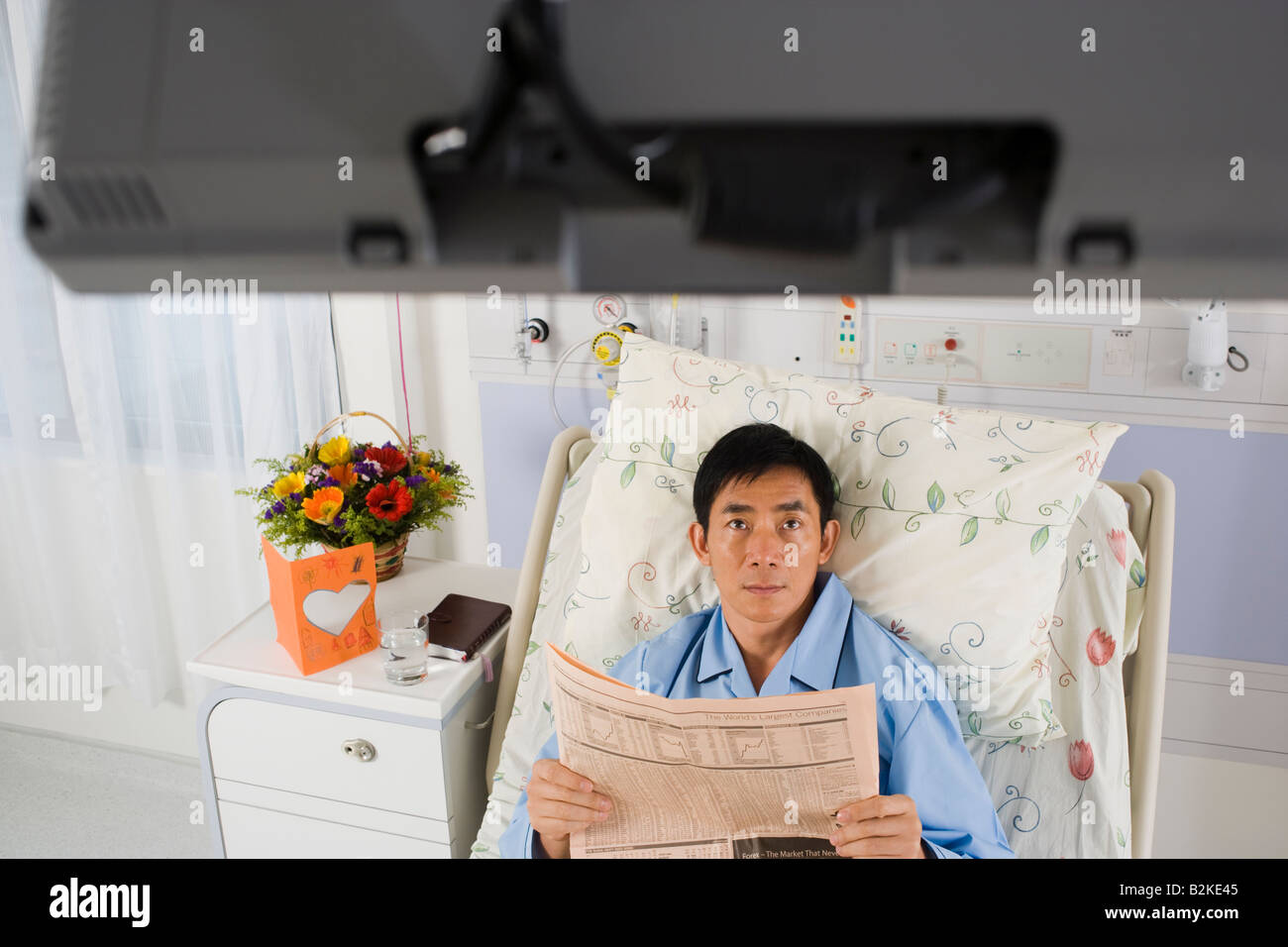 Tenant un journal du patient et à la recherche à la télévision dans un hôpital Banque D'Images
