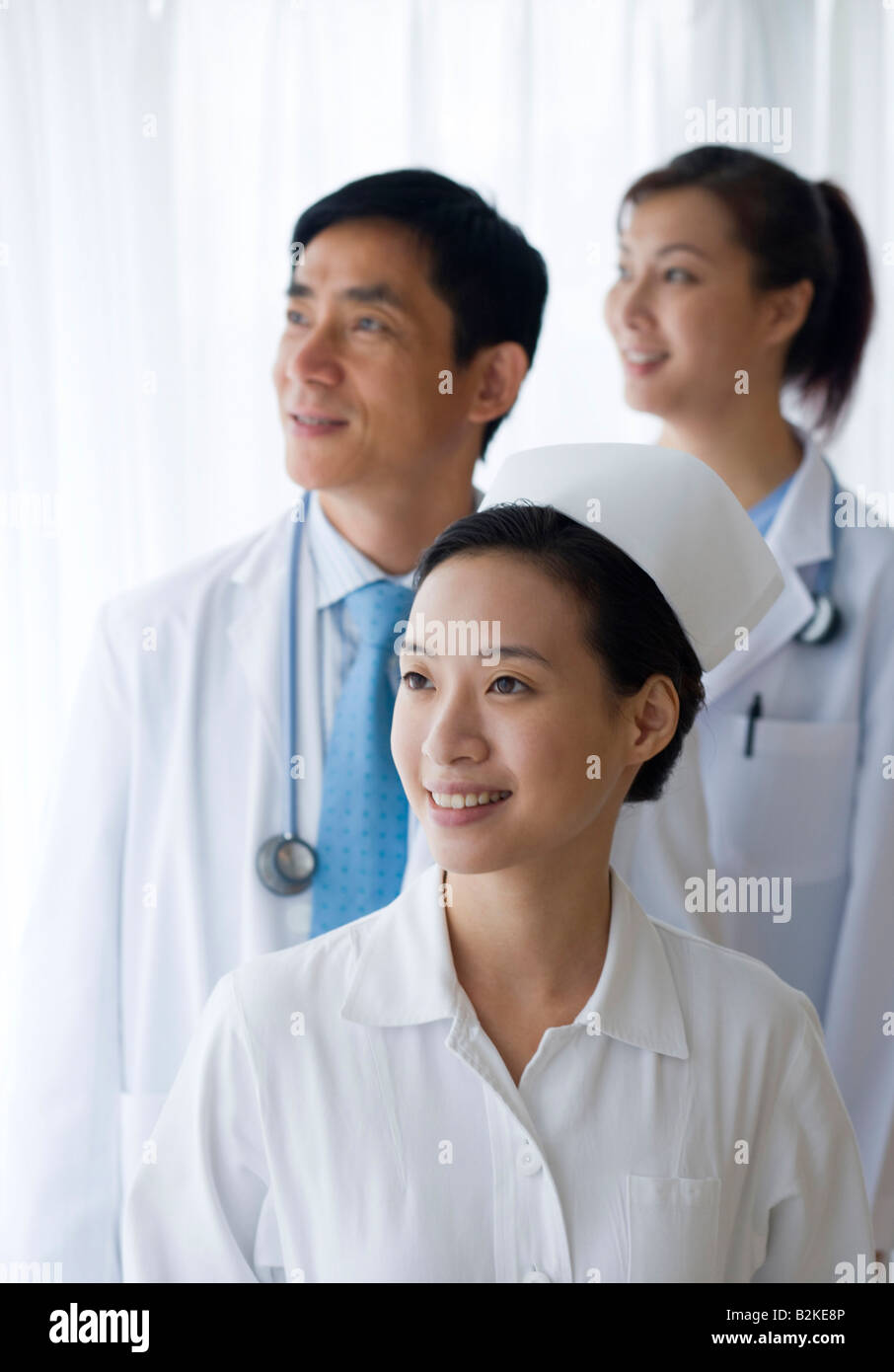 Nurse smiling avec deux médecins debout derrière elle Banque D'Images
