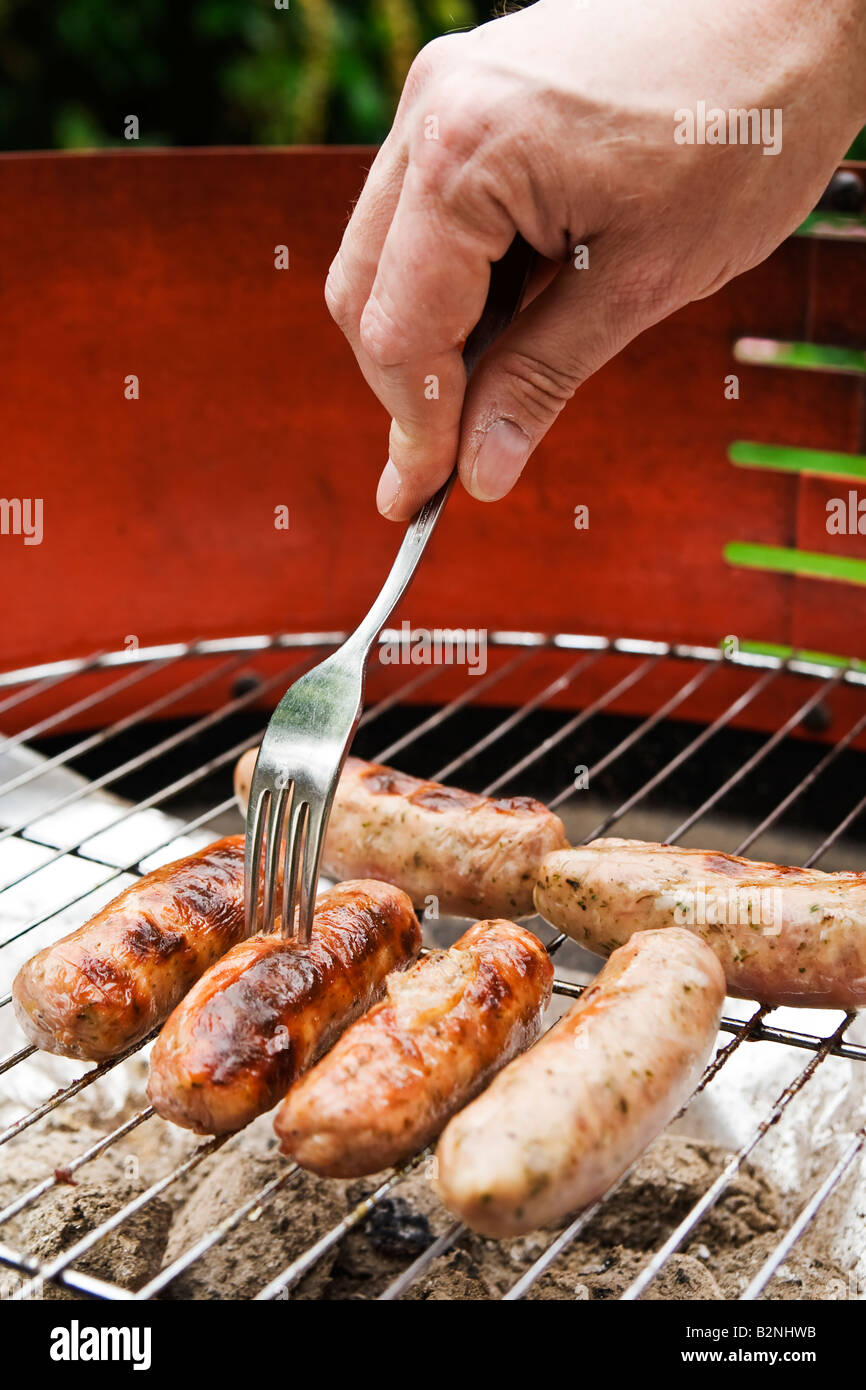 Man ^, piquer les saucisses sur le barbecue, UK. Banque D'Images