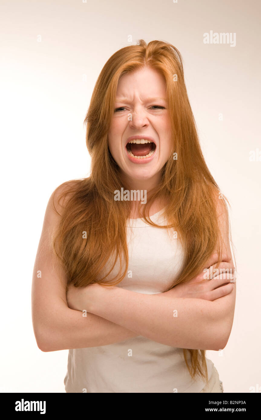 Rouge Long haired girl de 19 ans gilet blanc portant des cris de rage furieuse en colère, les bras croisés Banque D'Images