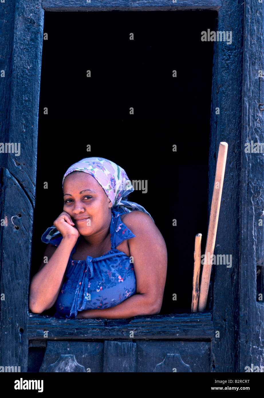 Jeune femme portant un foulard de Cuba, à la recherche d'un cadre en bois dans une porte, souriant à la caméra à Trinidad, Cuba Banque D'Images