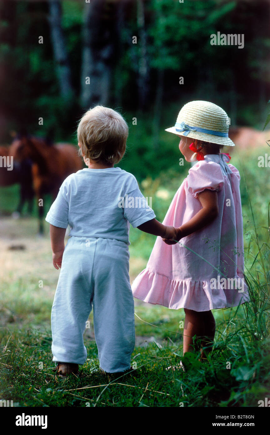 Garçon et fille de 2 à 3 ans se tenant la main dans le champ avec les chevaux de la Suède l'été Banque D'Images
