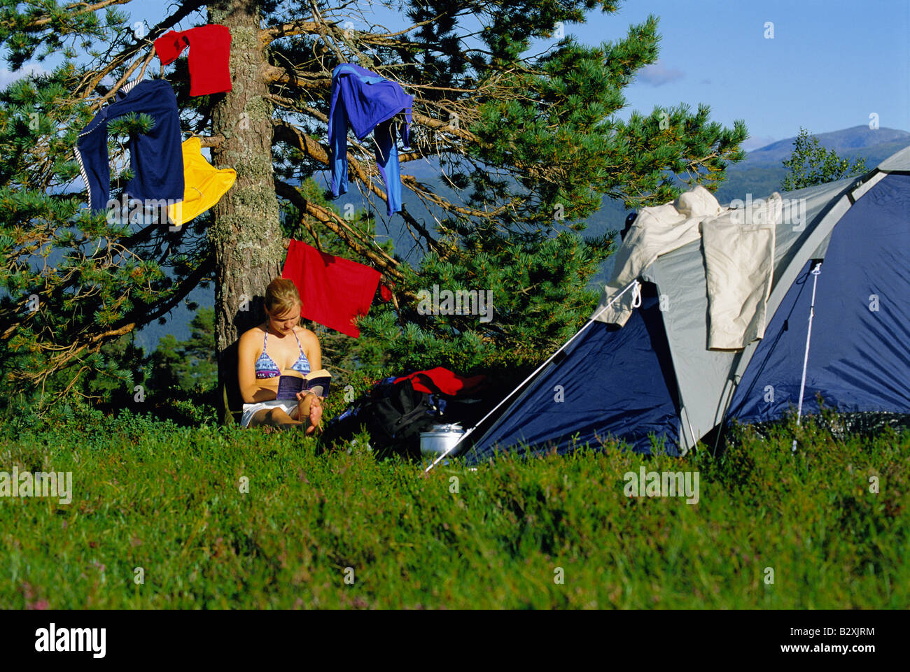 Femme en plein air au camping d'étendage par livre de lecture Banque D'Images