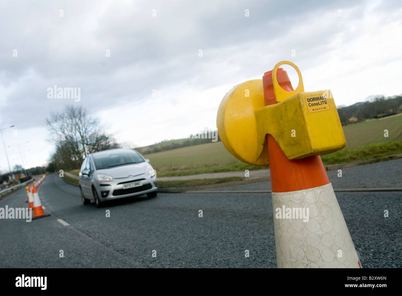 Une voiture passe un clignotant jaune au sommet d'un cône des travaux routiers au Royaume-Uni Banque D'Images