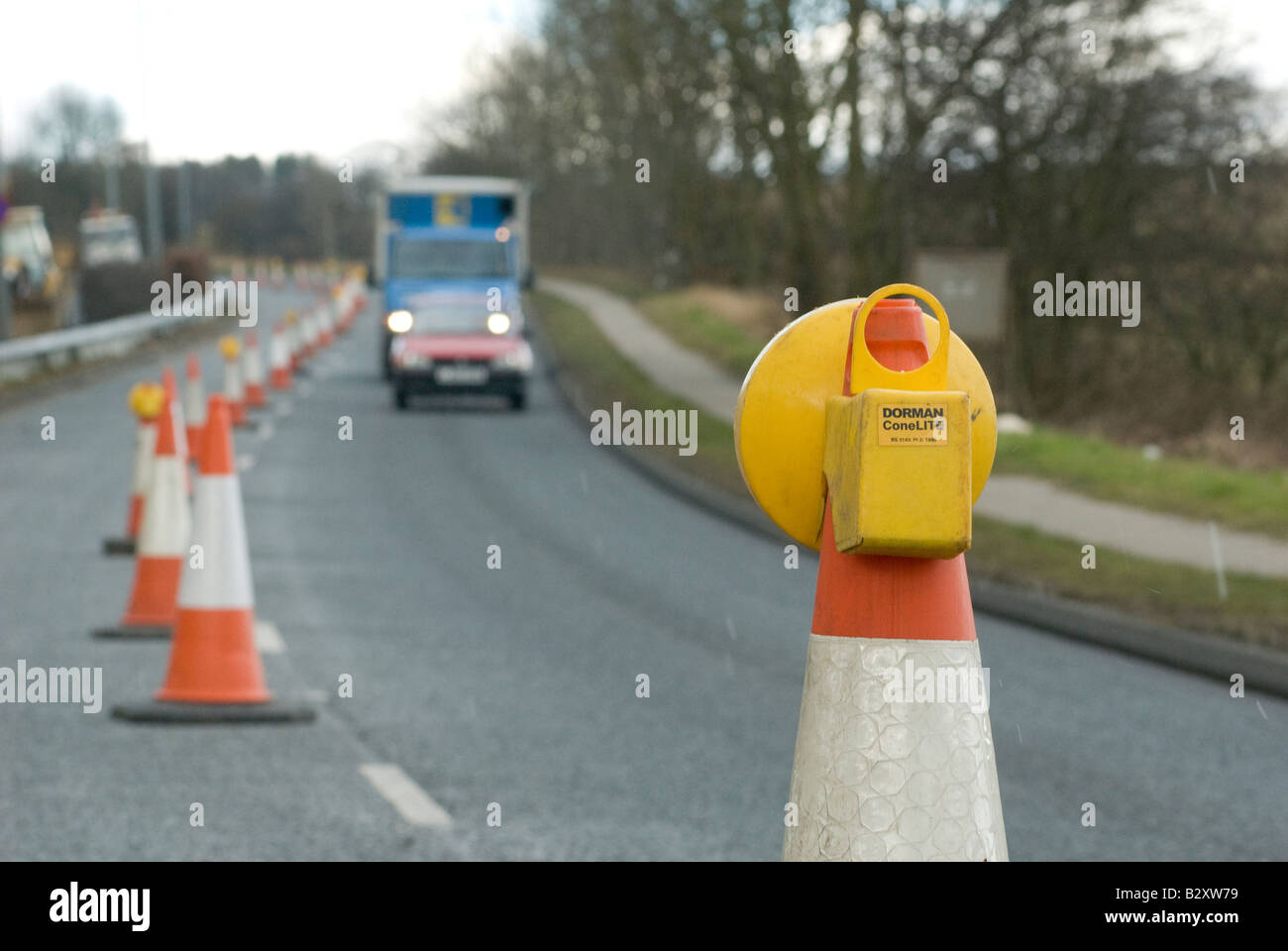 Le trafic passant un feu jaune clignotant sur le dessus d'un cône des travaux routiers au Royaume-Uni Banque D'Images