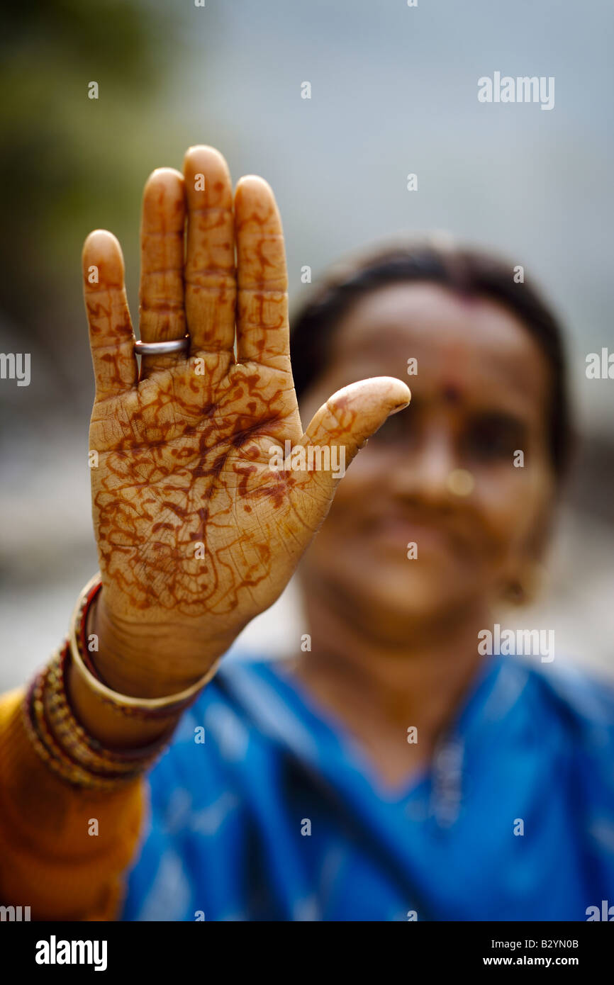 Une vue en gros plan d'une indienne's palm, ornés de tatouages au henné rouge et des bijoux. Le visage de la femme sourit de derrière. Banque D'Images