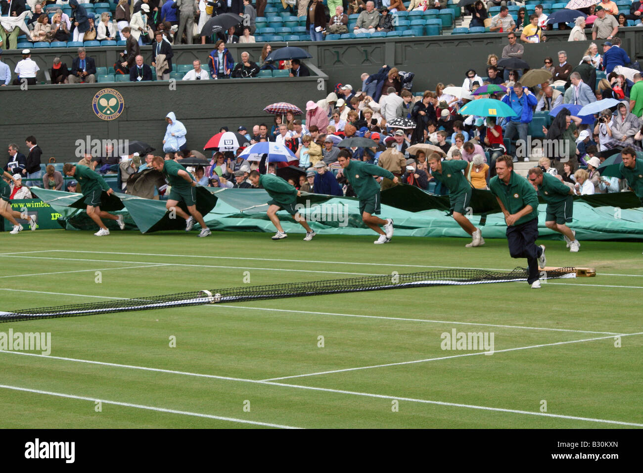 Le personnel au sol se précipiter pour placer le couvercle sur le court central au Championnat de Tennis de Wimbledon en Angleterre Banque D'Images