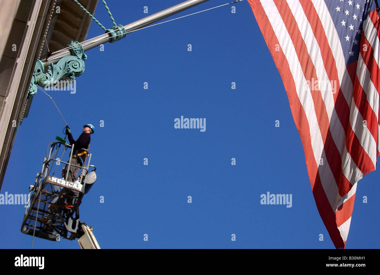 Un homme se lave vitres en hauteur sur un bâtiment comme un gigantesque drapeau américain se bloque contre un ciel bleu. Banque D'Images