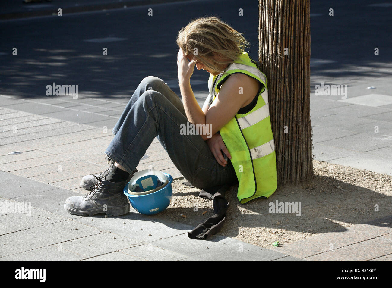 Épuisé construction worker assis sur le trottoir Banque D'Images
