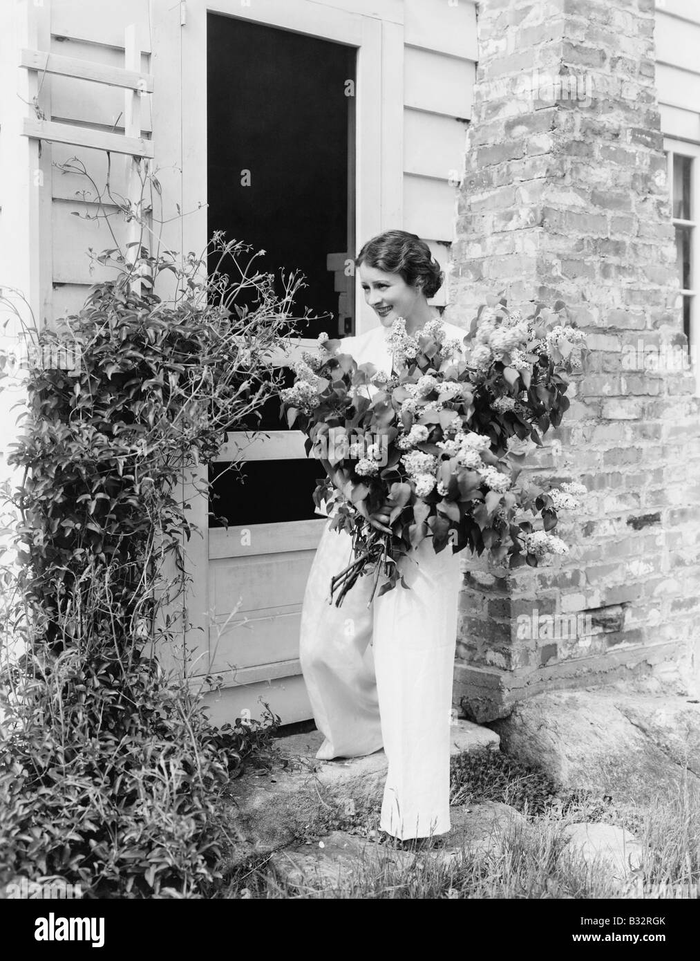 Femme devant sa maison des fleurs dans ses bras Banque D'Images