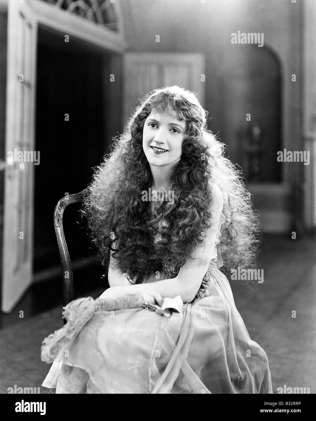 Jeune femme avec de longues boucles, cheveux bouclés, frisés assis sur une chaise et souriant Banque D'Images