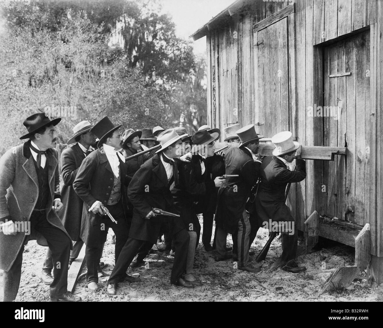 Groupe d'hommes en armes et chapeaux haut par effraction dans une grange Banque D'Images