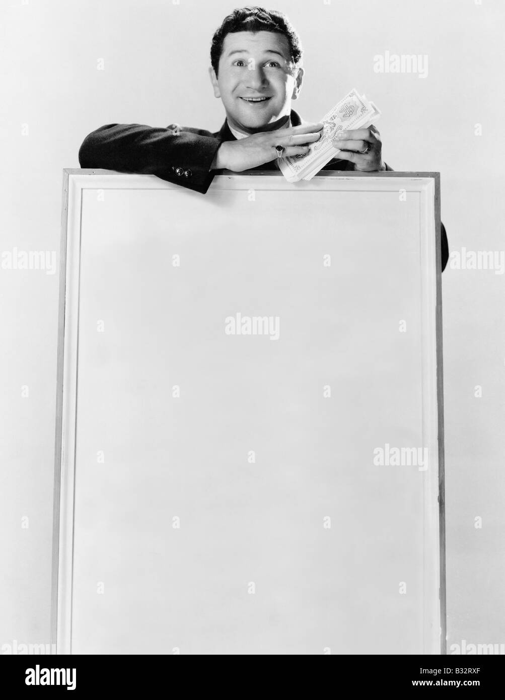 Homme debout derrière un panneau d'information et la tenue de liasses de billets de monnaie Banque D'Images