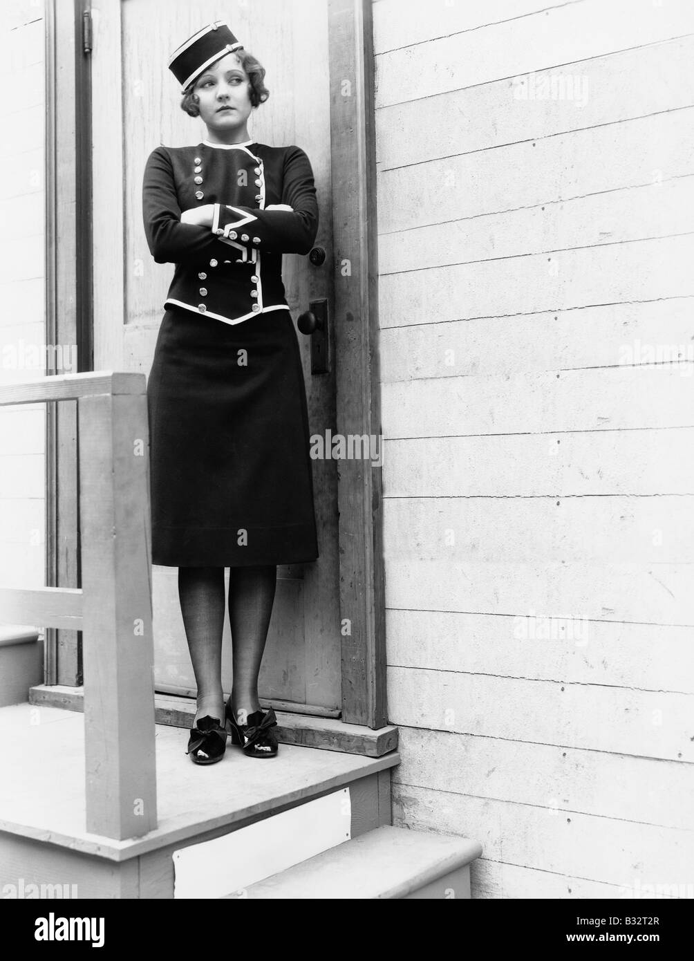 Jeune femme en uniforme debout avec les bras croisés devant une porte fermée Banque D'Images