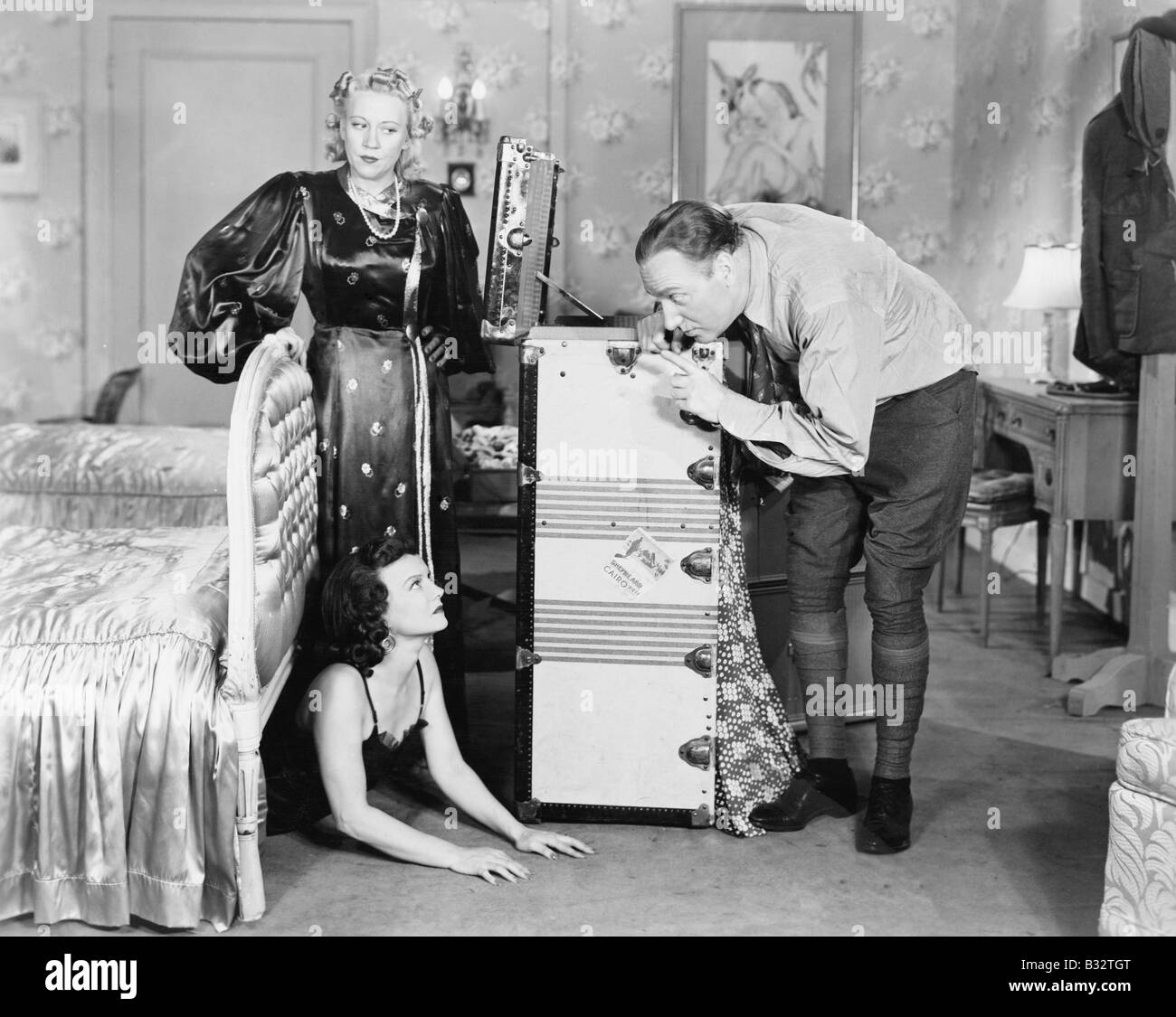 Jeune femme se cacher sous un lit et un couple debout près de sa Banque D'Images