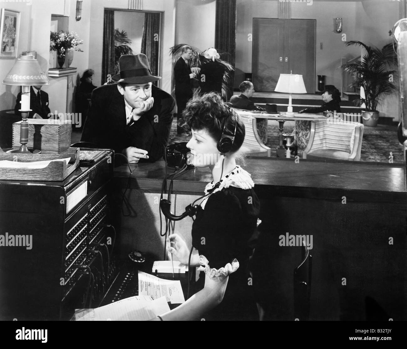 Profil d'une femme au travail sur le standard téléphonique avec un homme la regardant Banque D'Images