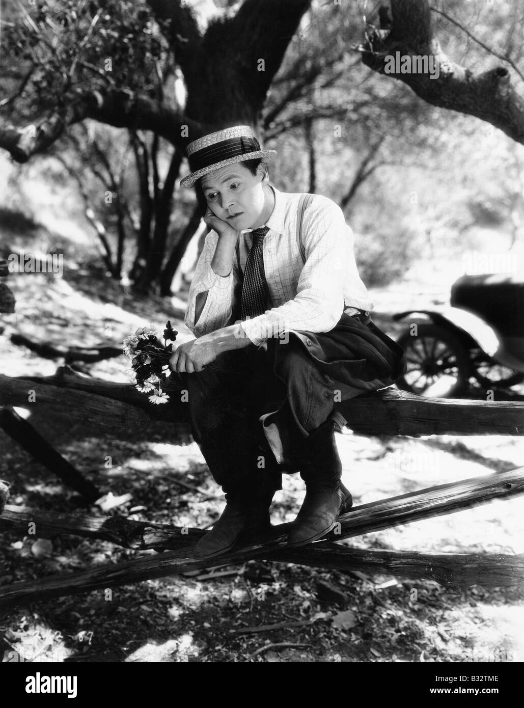 Homme assis sur une clôture avec des fleurs dans ses mains et à la triste Banque D'Images