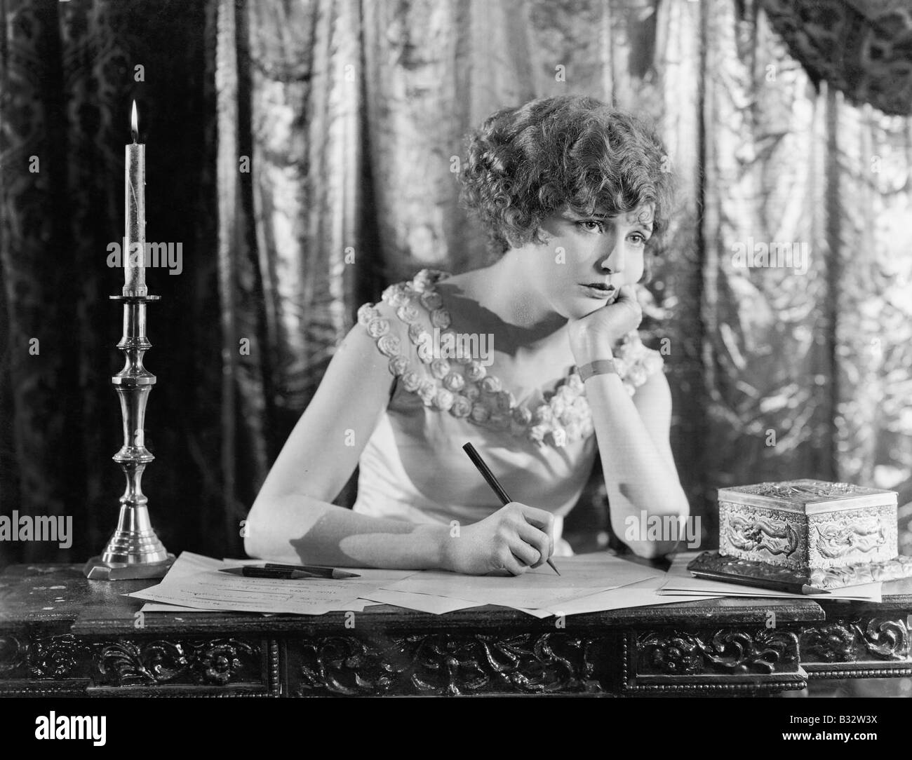 Jeune femme assise à un bureau avec un stylo à la main, à la triste tout en écrivant une lettre Banque D'Images