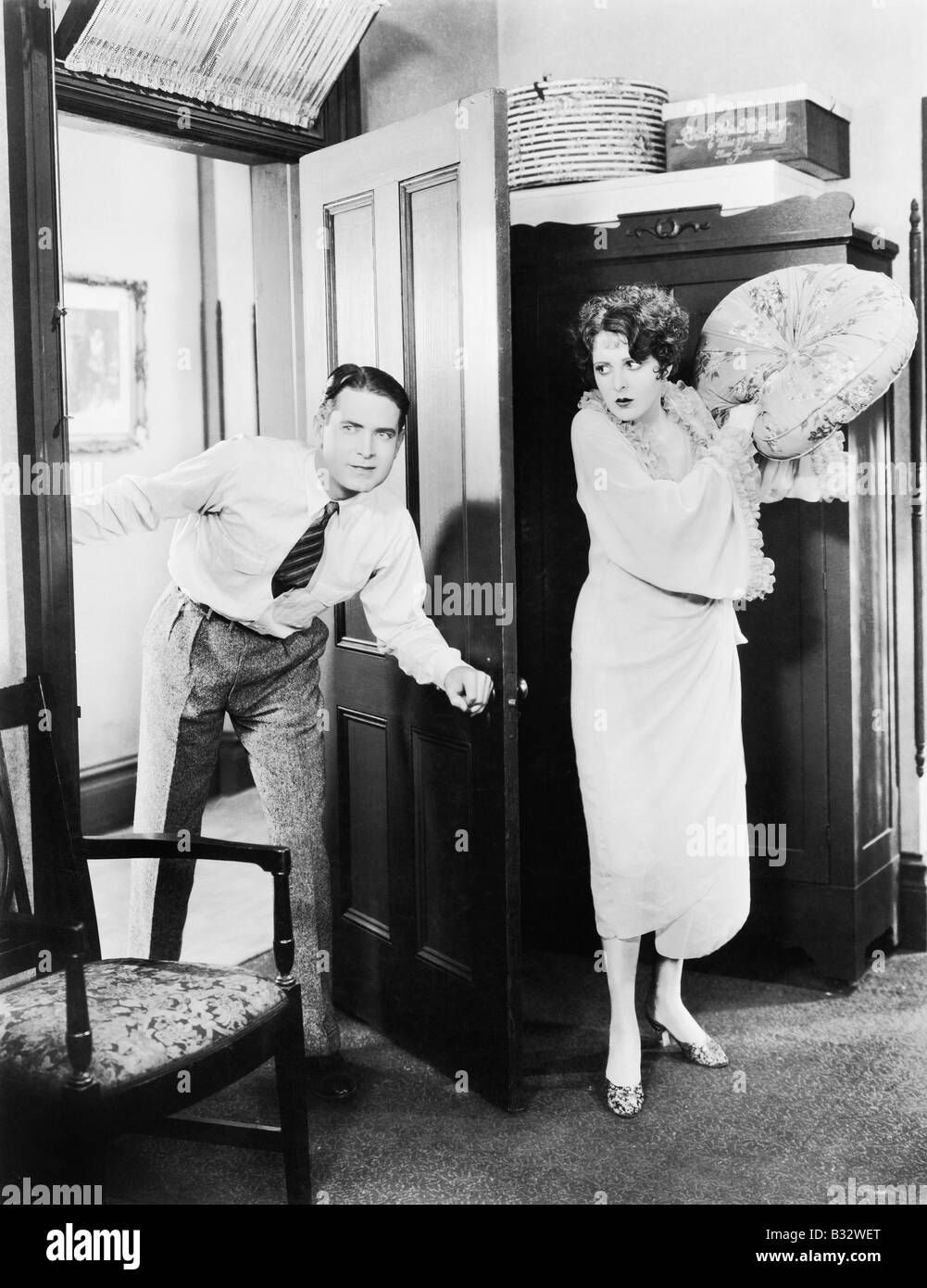 Femme debout derrière une porte en tentant de frapper un homme avec un oreiller Banque D'Images