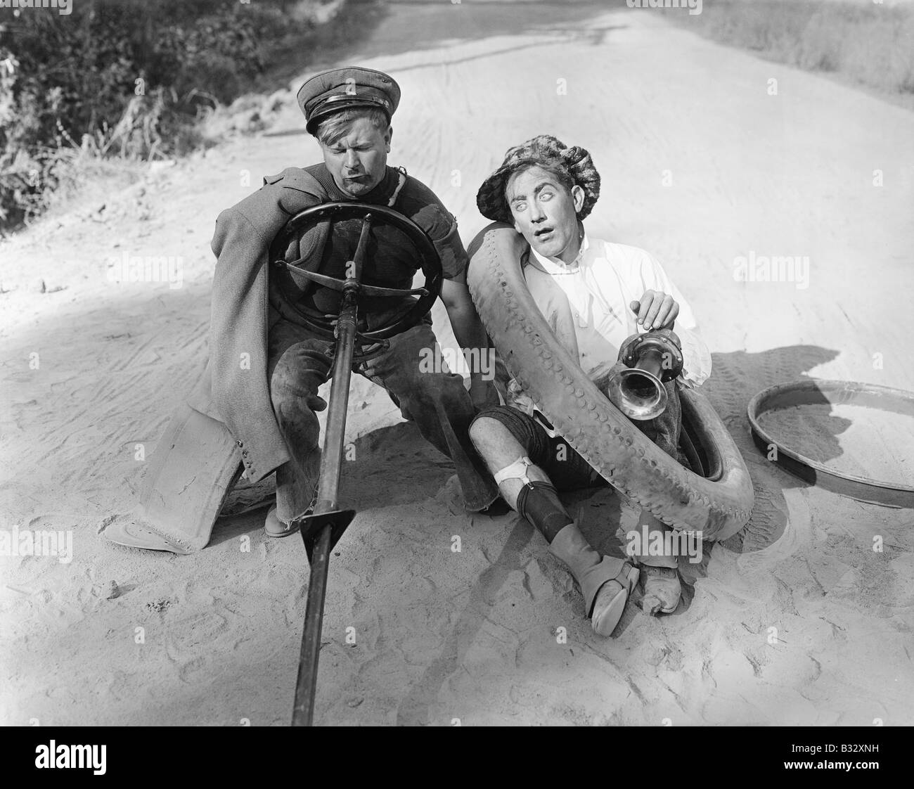 Deux hommes assis sur un sol fait semblant de conduire une voiture avec des pièces de voiture Banque D'Images