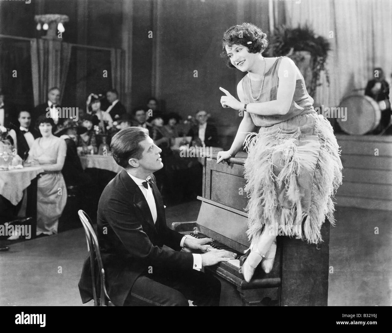 Jeune femme assise sur un piano et parler avec le pianiste Banque D'Images
