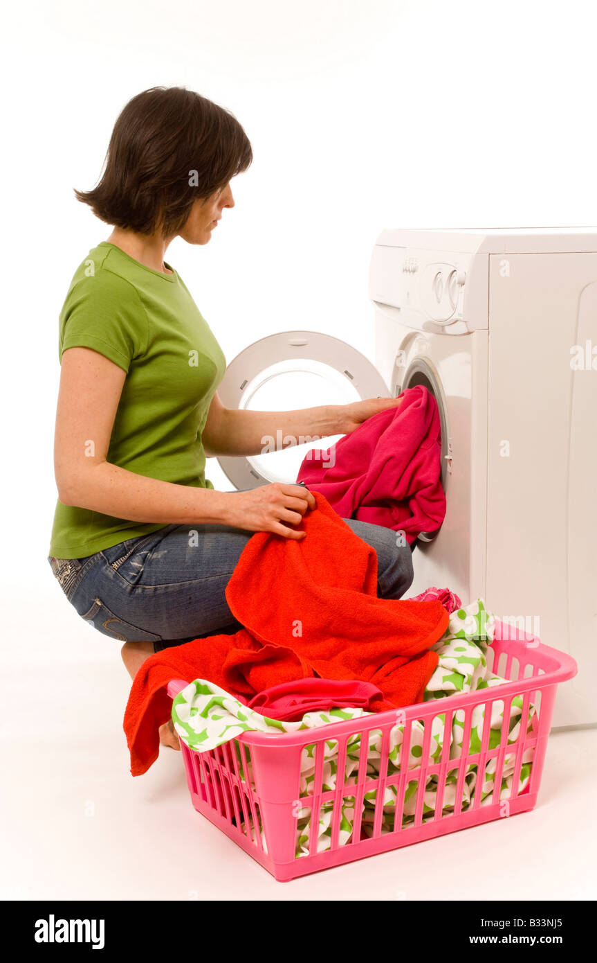 Jeune femme caucasienne portant un t-shirt vert et un Jean chargeant un lave-linge domestique avec des vêtements de couleurs vives provenant d'un panier à linge. Banque D'Images