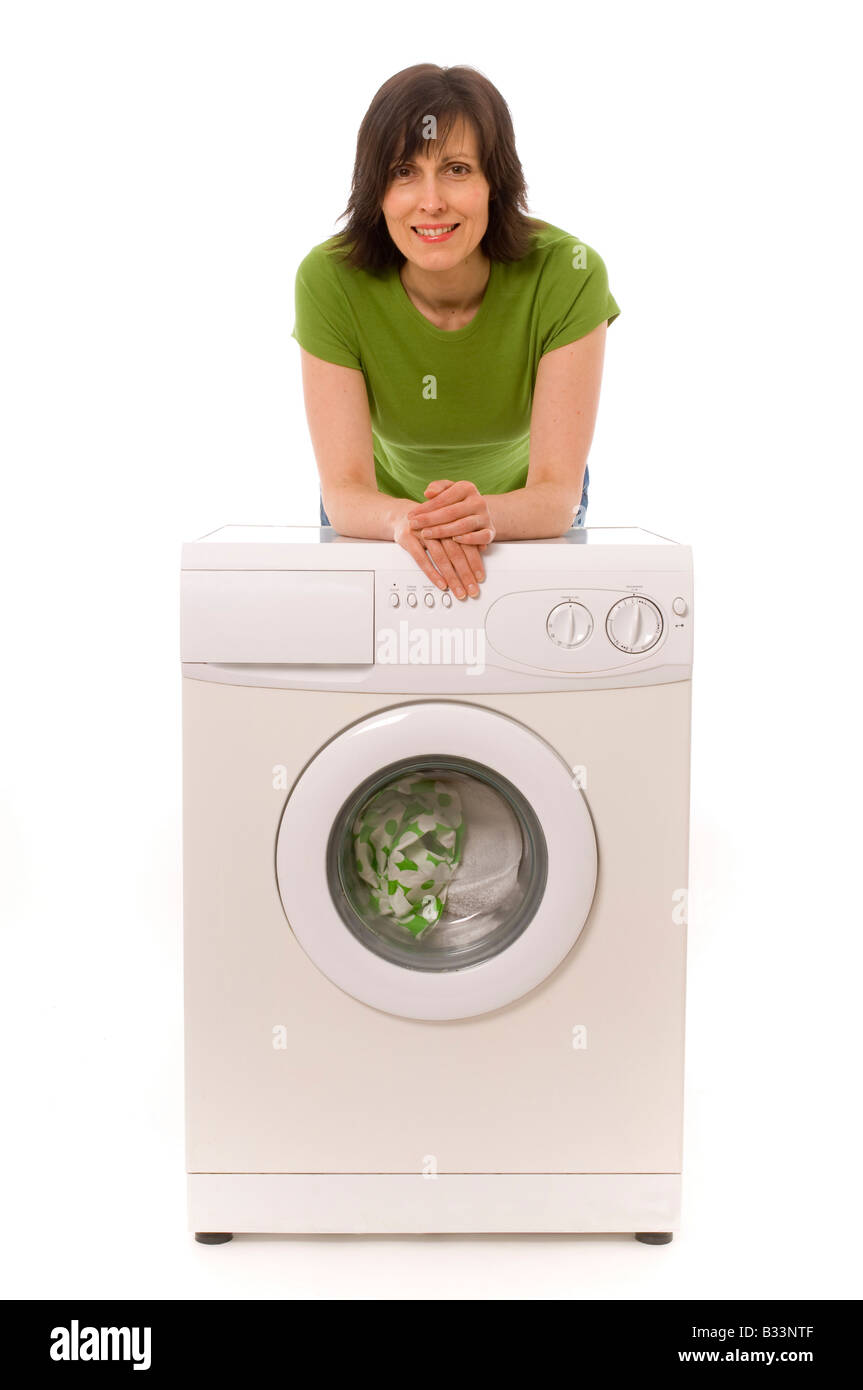 Femme caucasienne portant un haut vert penchée sur un lave-linge domestique souriant et heureux. Banque D'Images