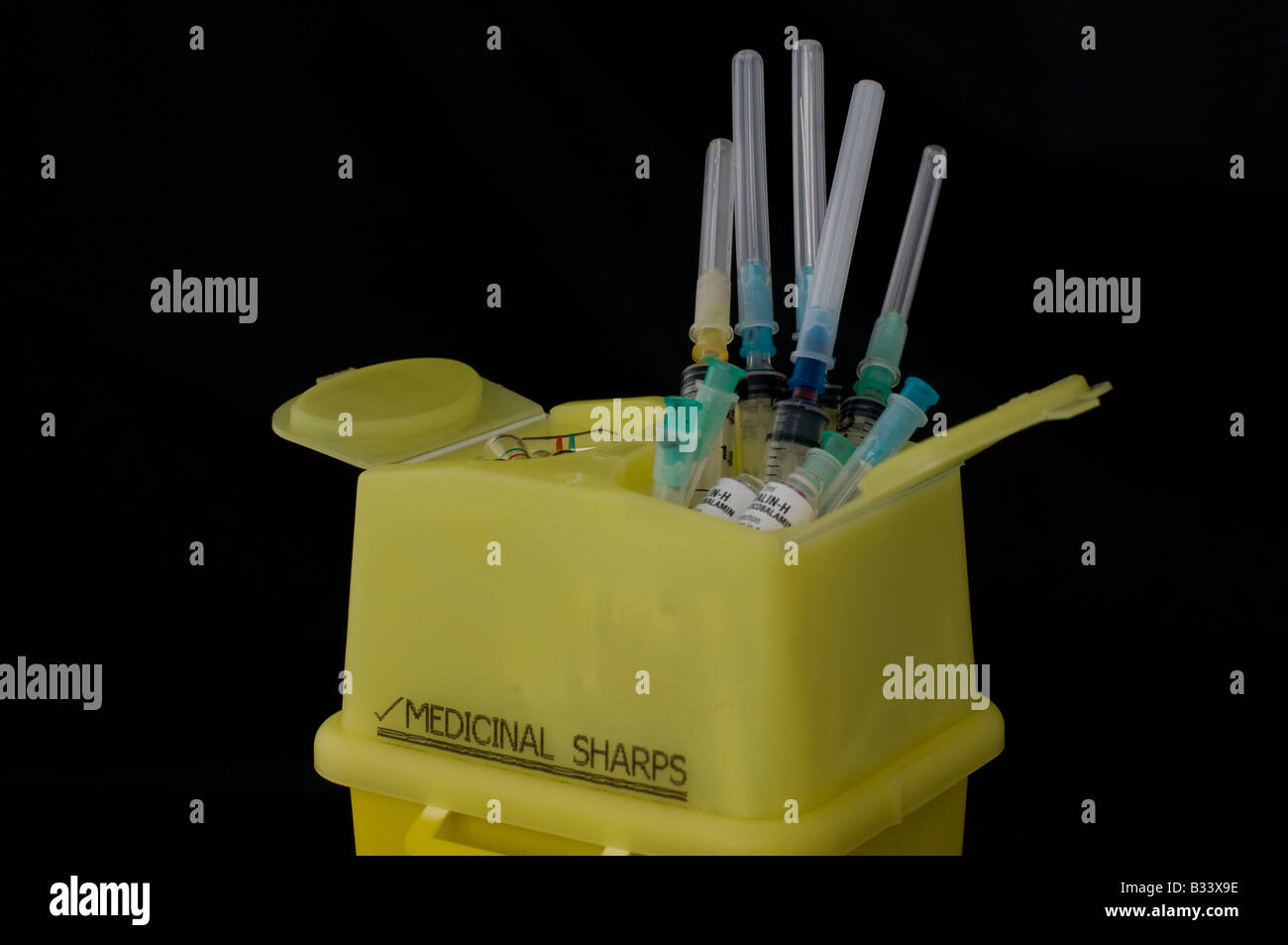 Les aiguilles et seringues hypodermiques stick à partir d'une boîte pour objets tranchants à être éliminés comme déchets cliniques. Banque D'Images