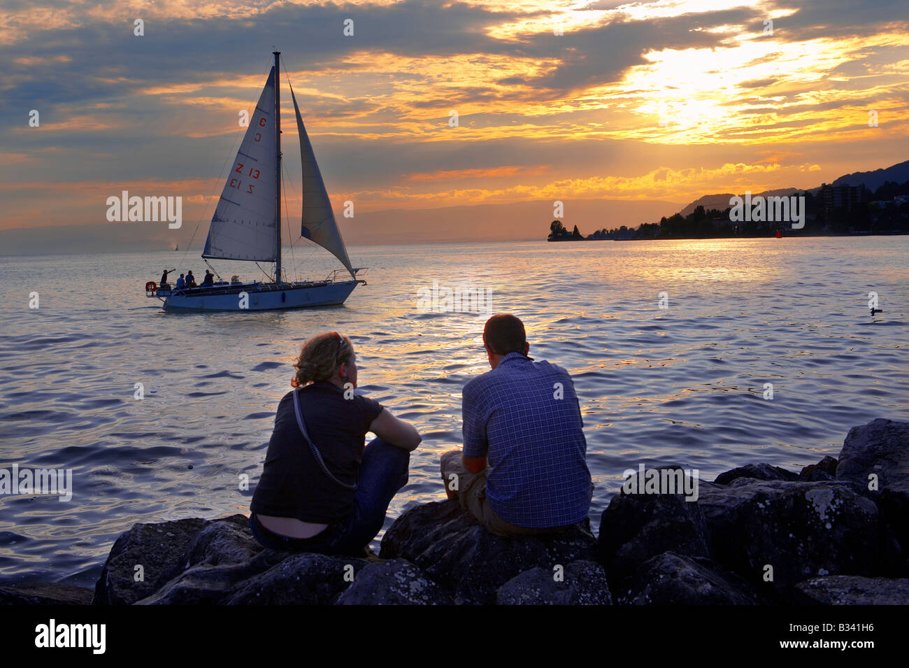 Bateau à voile sur le Lac Léman au coucher du soleil avec un jeune couple silouetted, Montreux, Vaud Suisse Banque D'Images