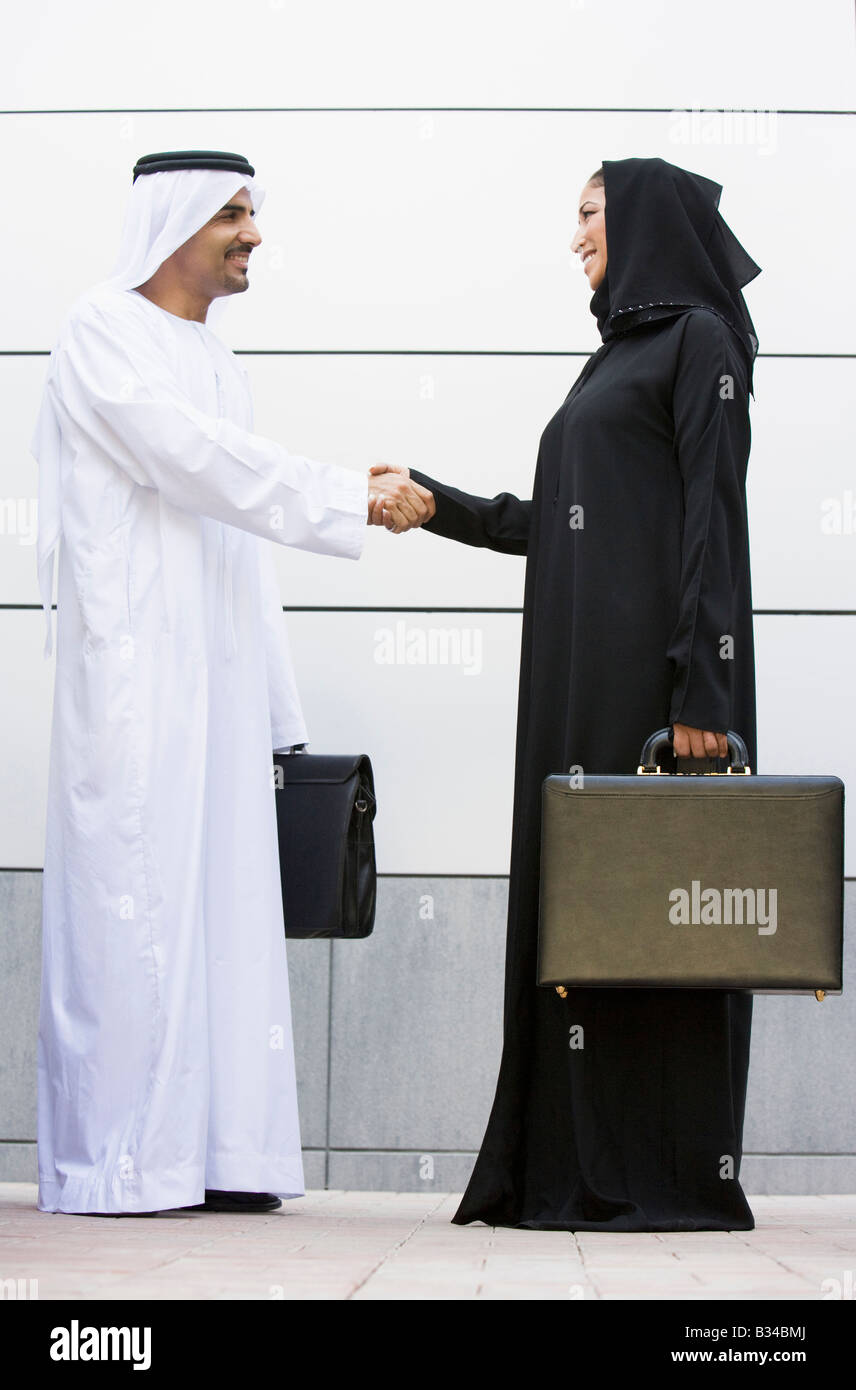 Deux businesspeople standing en plein air avec porte-documents shaking hands and smiling Banque D'Images