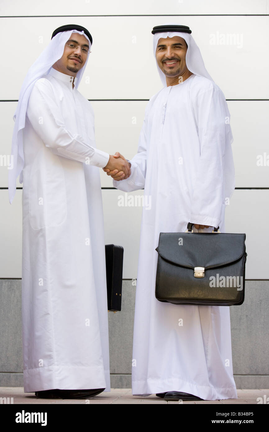 Deux businessmen standing en plein air avec porte-documents shaking hands and smiling Banque D'Images