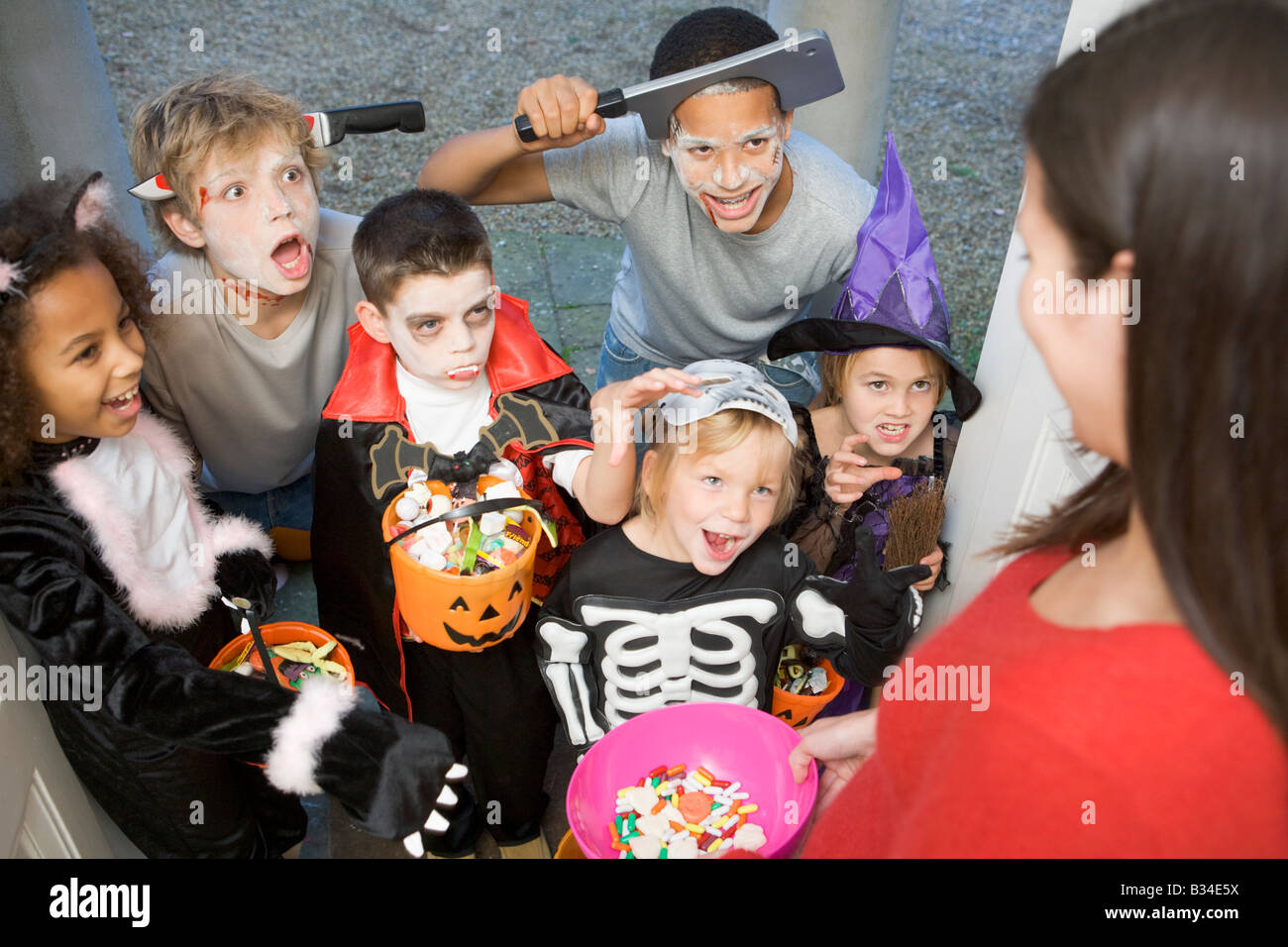 Six enfants en costumes trick or treating at woman's house Banque D'Images