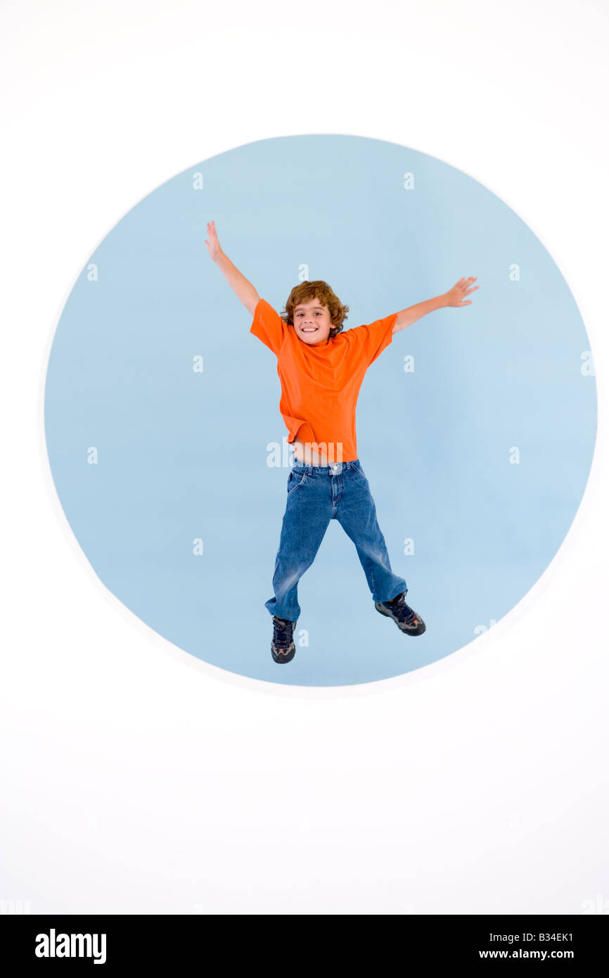 Jeune garçon sautant avec bras smiling Banque D'Images