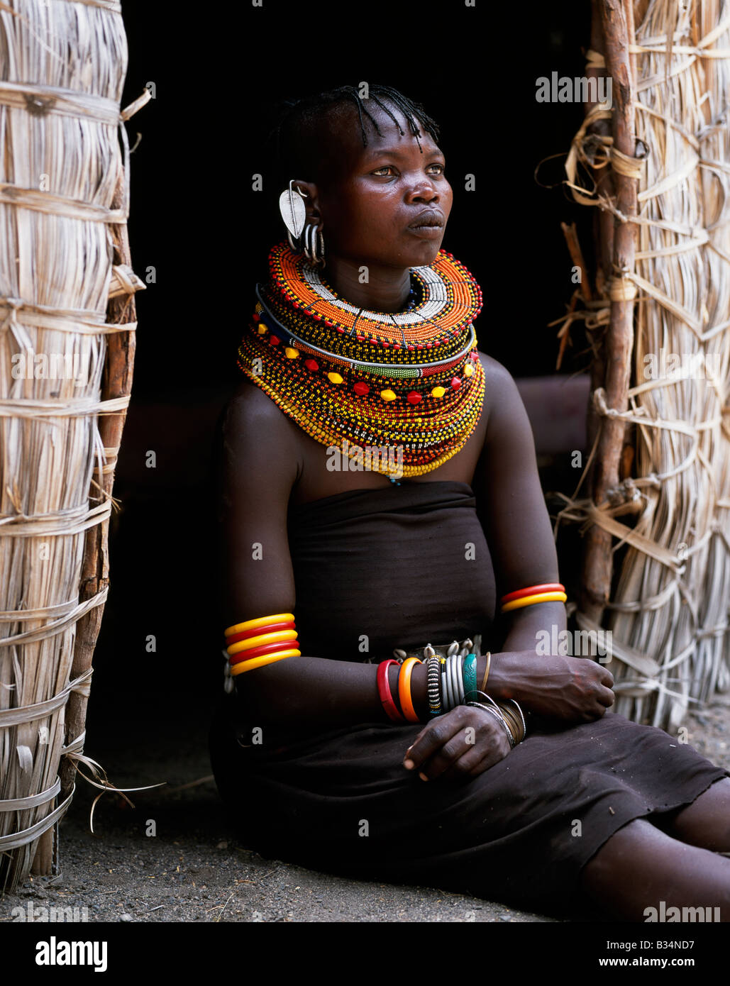 Kenya, Northern Frontier District, Loyangalani. Une femme Turkana,  généralement porter plusieurs couches de colliers de perles et d'une série  d'articles d'une paire d'earrrings en forme de feuille à l'avant, siège à  l'entrée