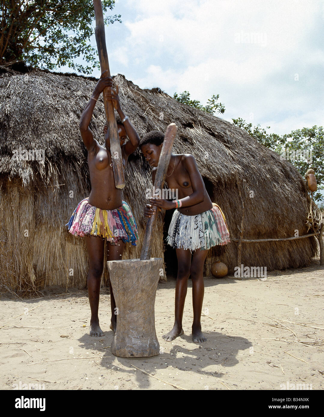 Kenya, Malindi, Gongoni. Deux filles Giriama pound le maïs de l'extérieur de leur foyer à l'aide d'un grand mortier en bois et les pilons. Banque D'Images